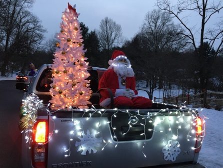 A full size fake Santa Claus sitting next to a white christmas tree display on a car