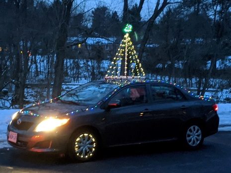 A wired Christmas tree with white lights on top of a car in the parade